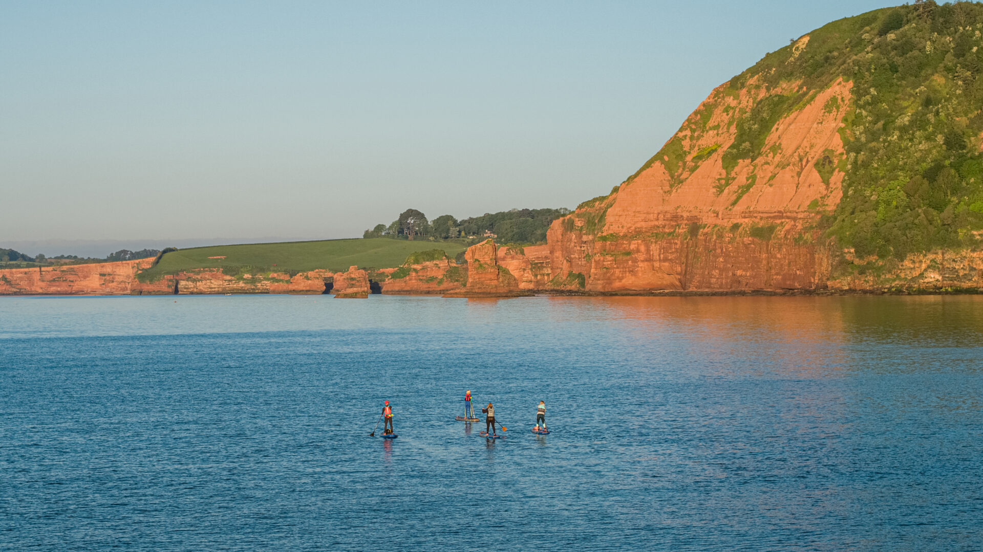 Paddle boarders in sea with golden cliffs of Sidmouth